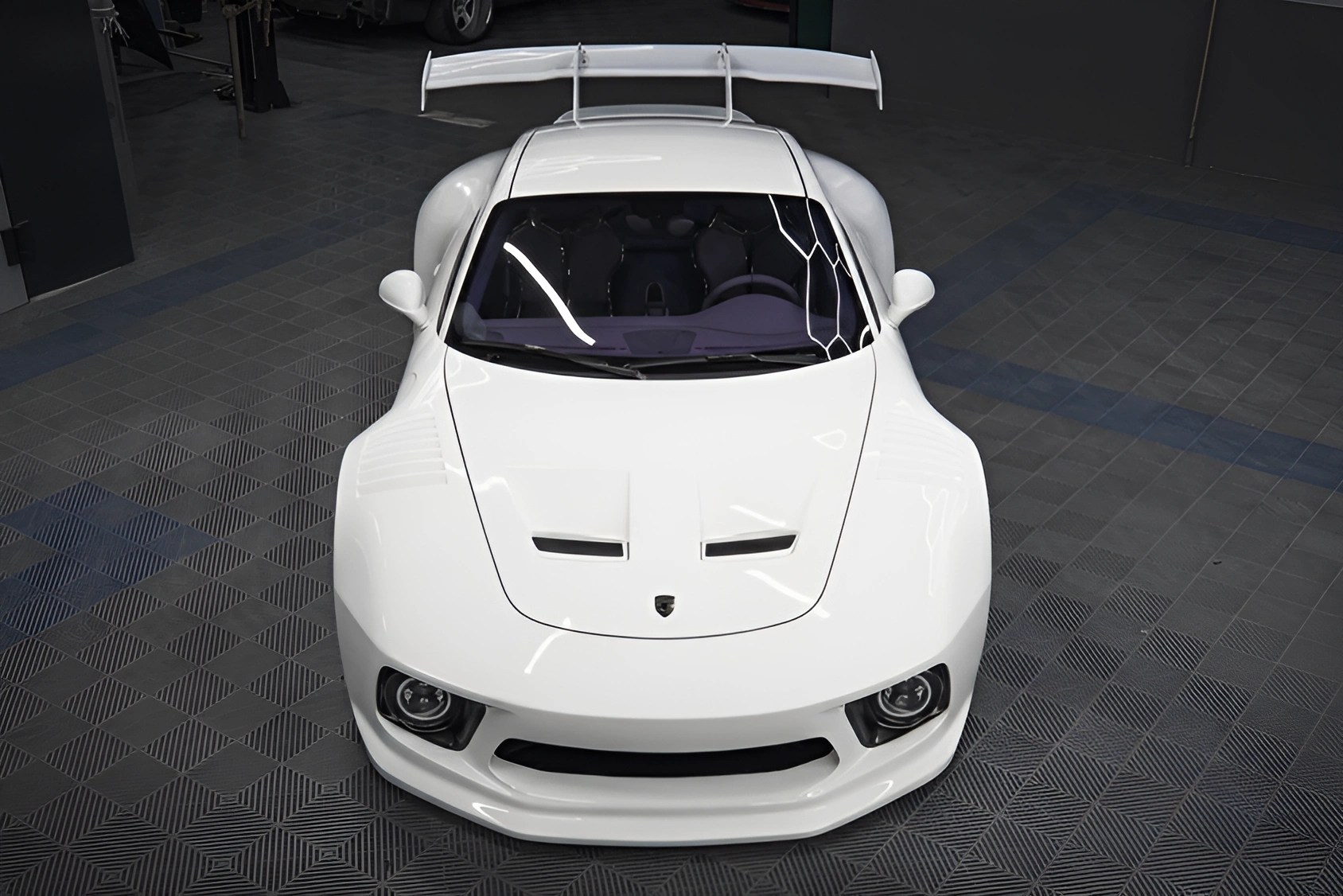 White sports car with wide body, large rear wing, and black headlights on a checkered floor.