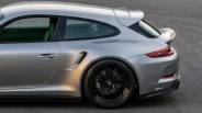 Silver sports car rear side with black alloy wheel and rear spoiler on asphalt surface.