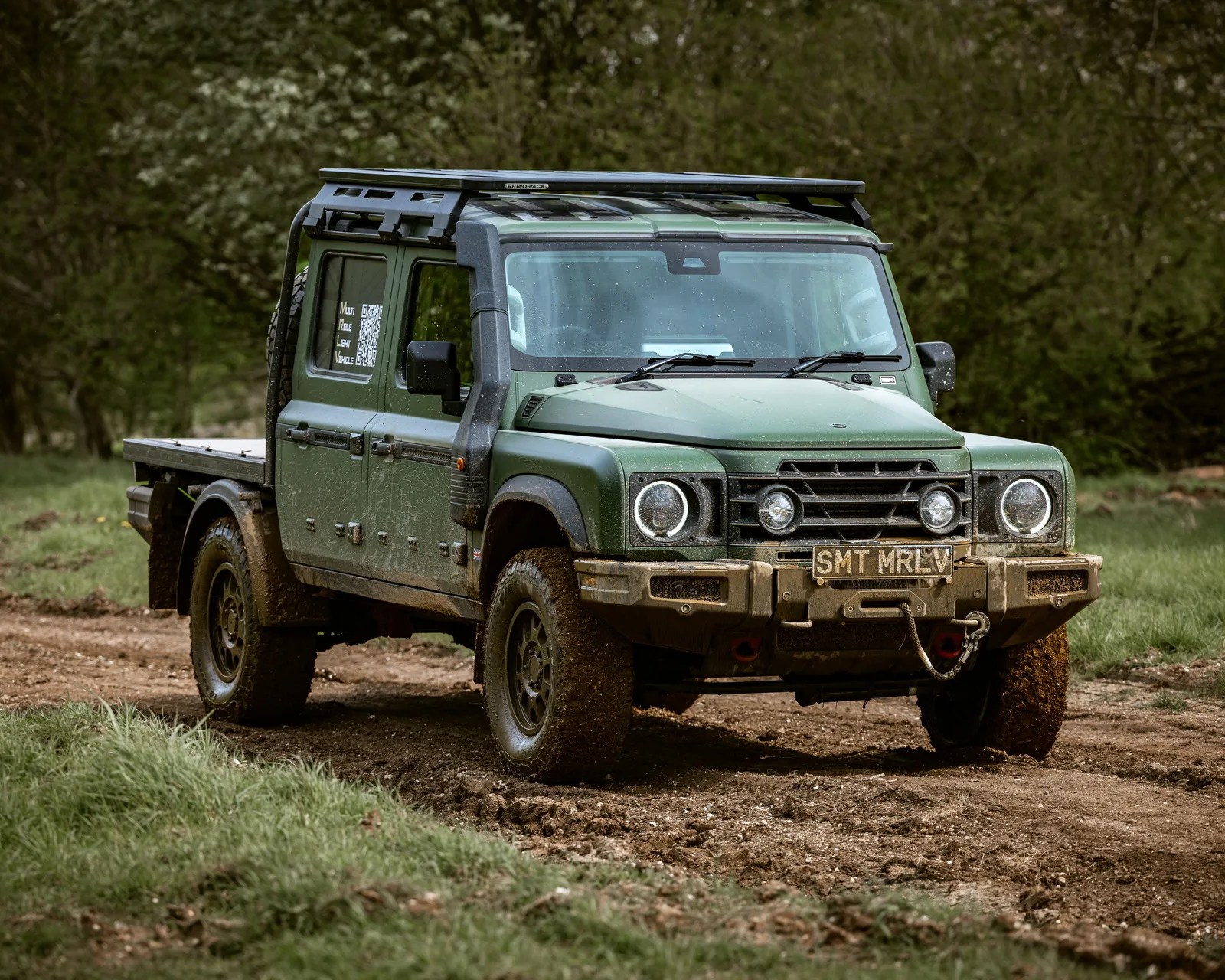 Green off-road pickup truck with roof rack and mud-covered tires on a dirt path.