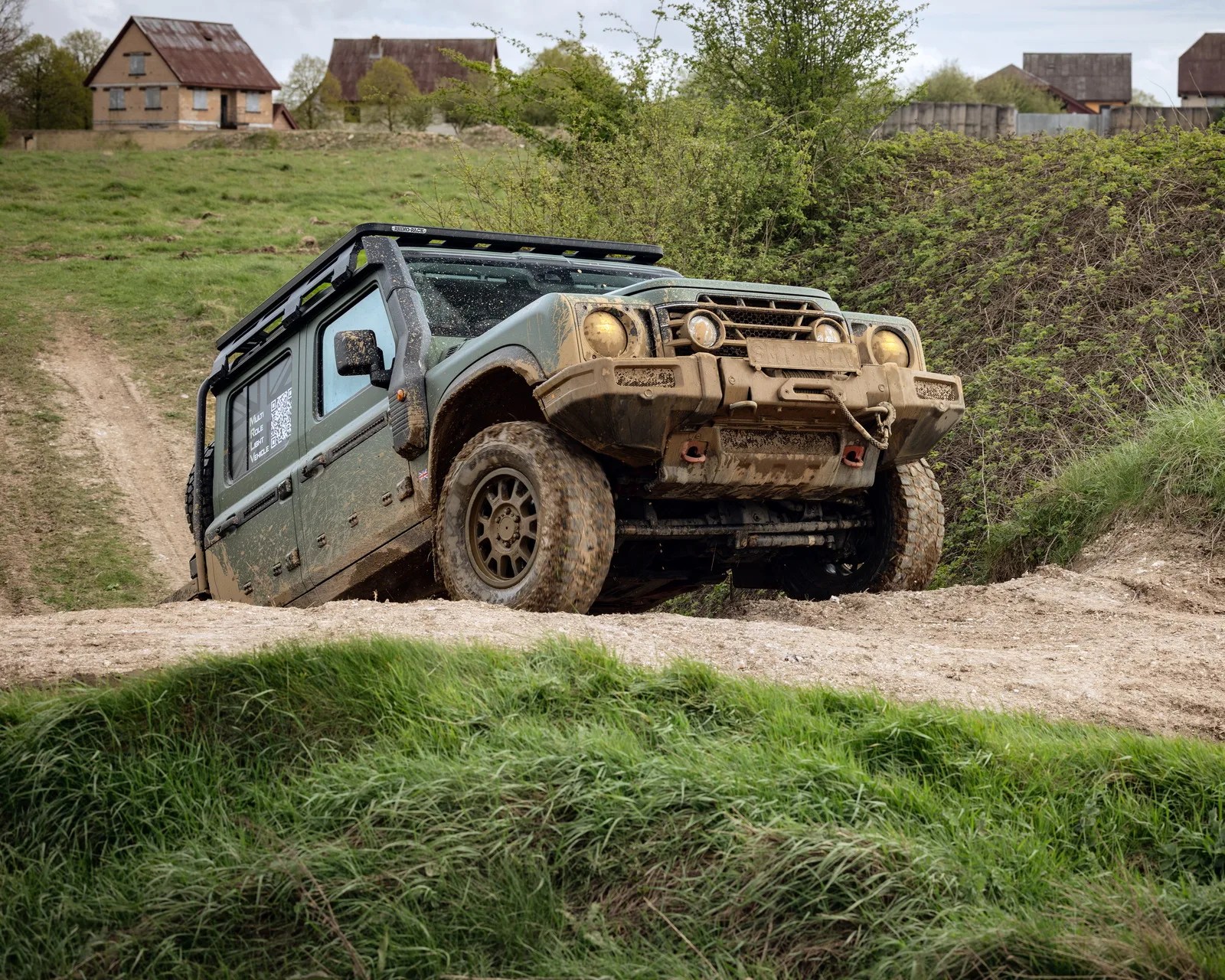 Green off-road SUV with mud splatters climbing a dirt hill in a rural area.
