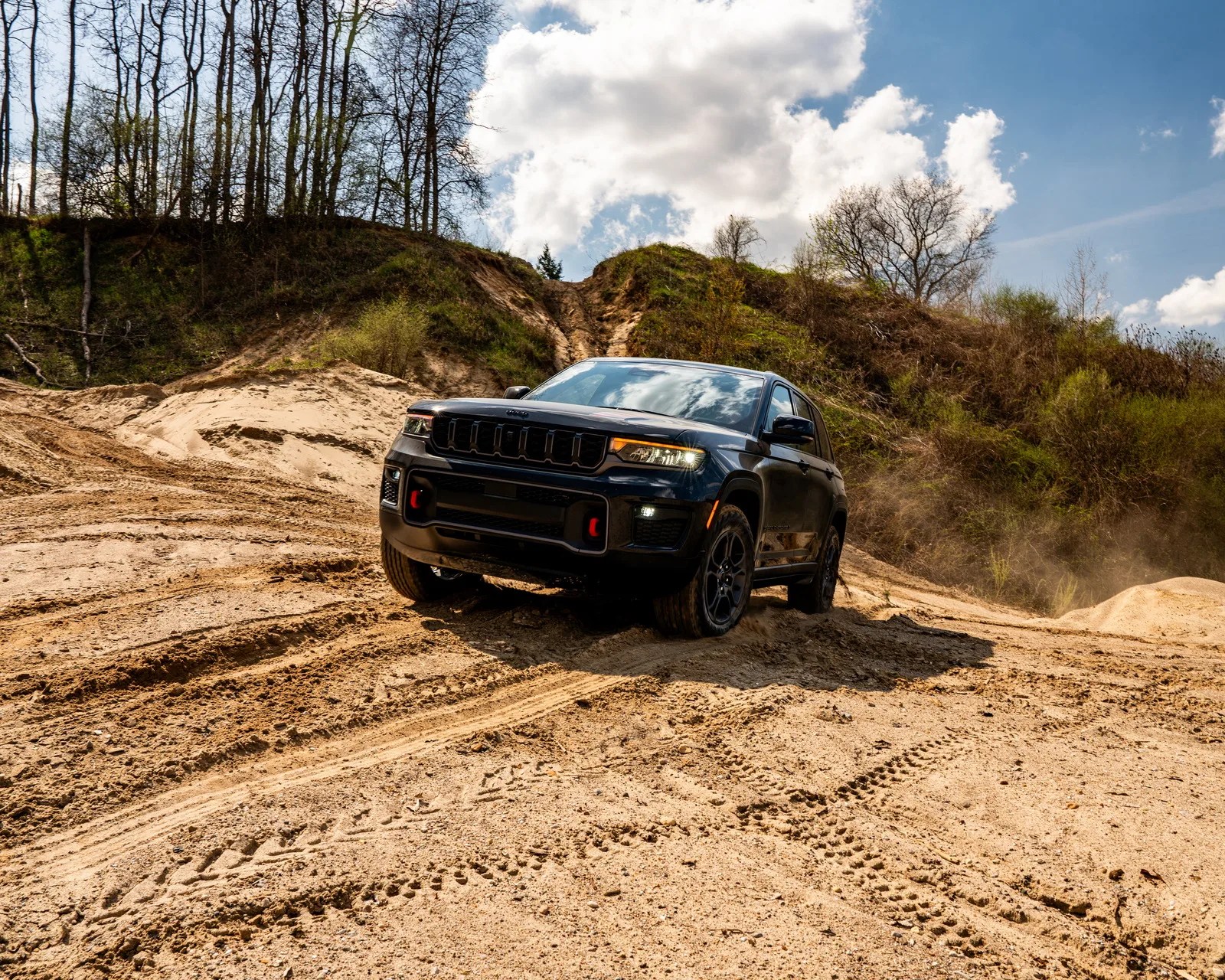 Black Jeep SUV driving on a sandy off-road trail with trees and a cloudy sky in the background.
