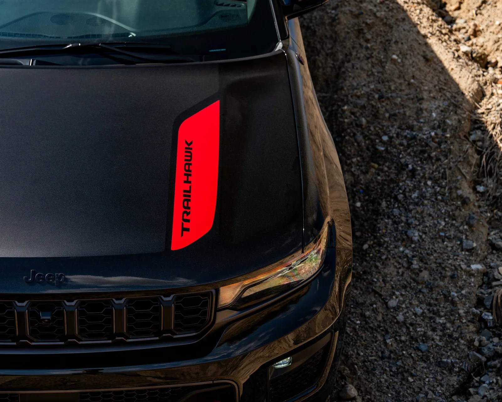 Black Jeep vehicle hood with a red "TRAILHAWK" decal on the right side, parked on gravel.