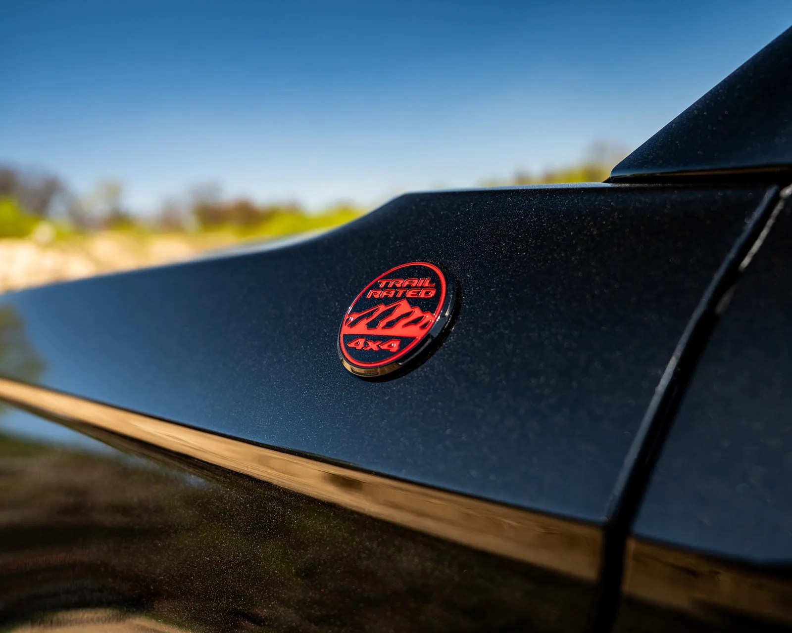 Red "Trail Rated 4x4" badge on a black vehicle panel with a blurred outdoor background.