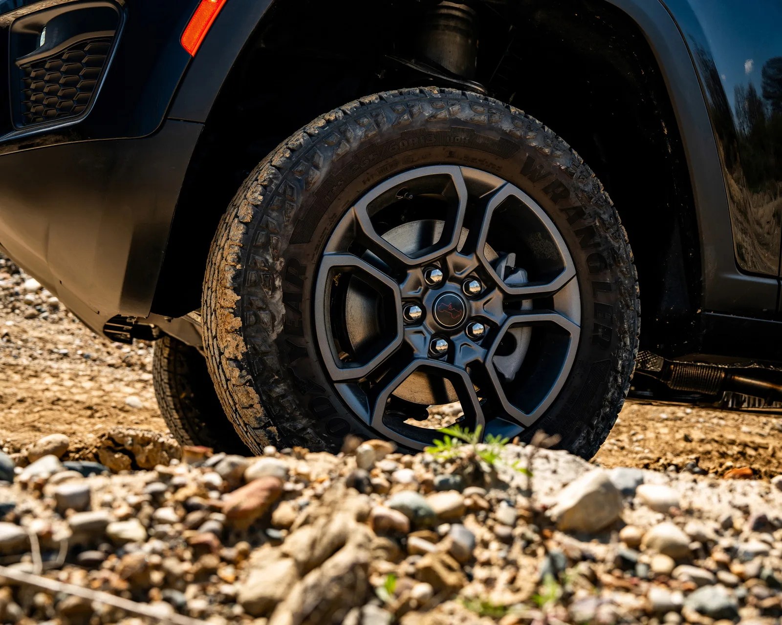 Black off-road tire with rugged tread mounted on a matte black alloy wheel on a vehicle on rocky terrain.