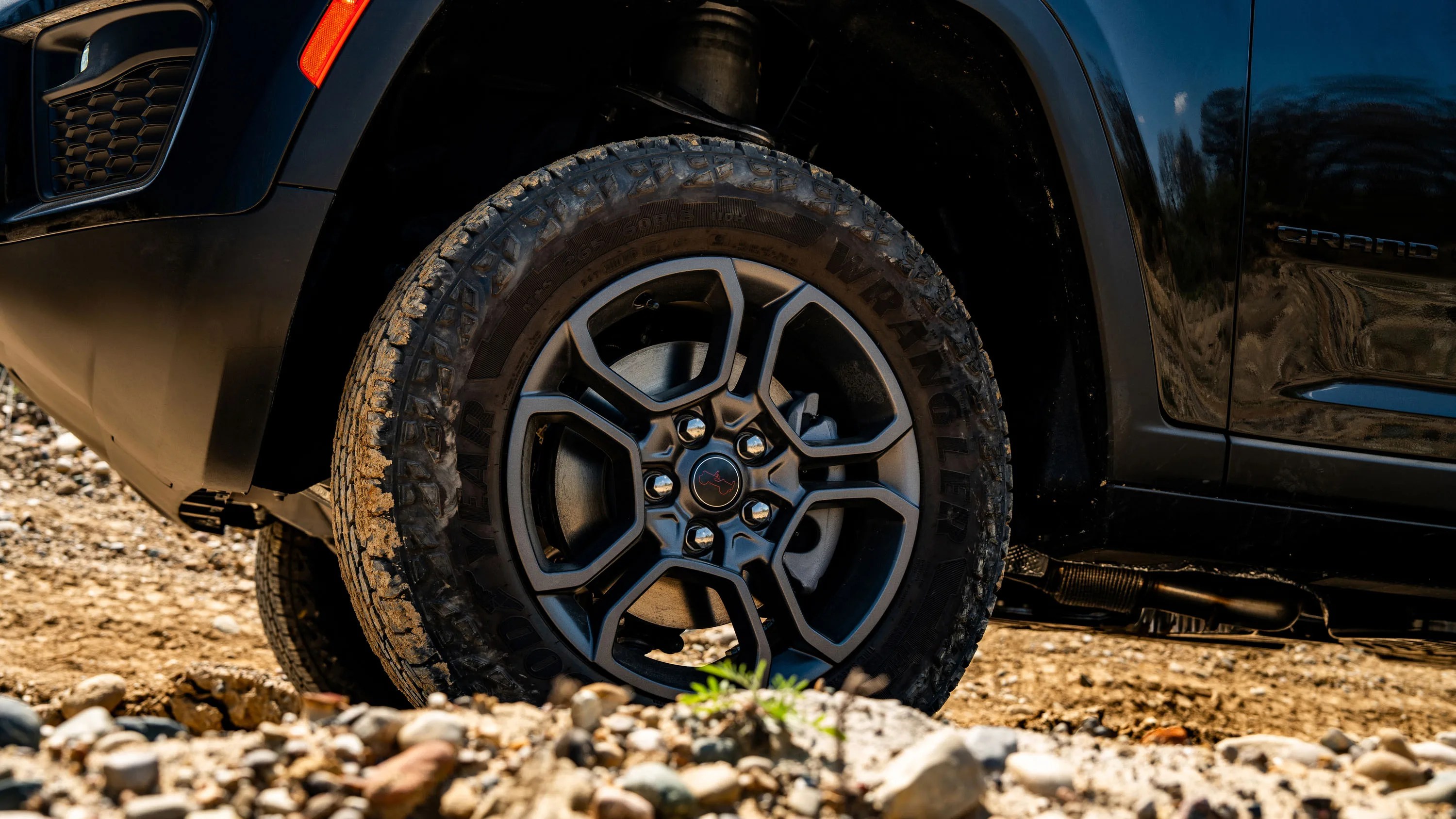 Off-road tire with black alloy wheel on a black vehicle on rocky terrain.