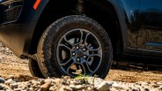 Off-road tire with black alloy wheel on a black vehicle on rocky terrain.