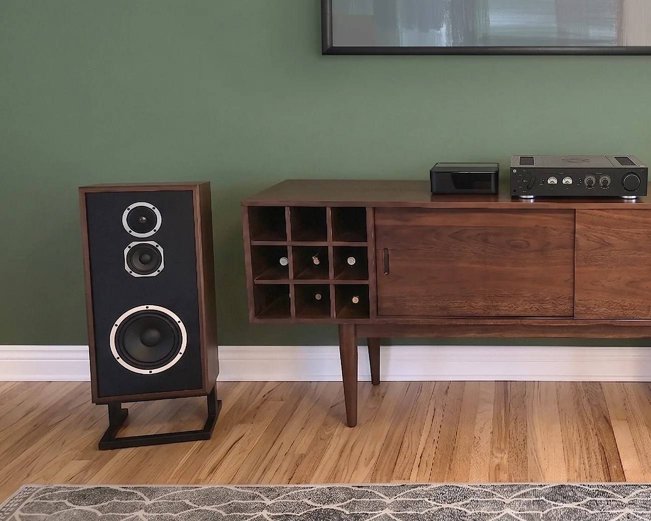 Mid-century wooden sideboard with built-in wine rack, vintage speaker on stand, and audio equipment on top against a green wall.