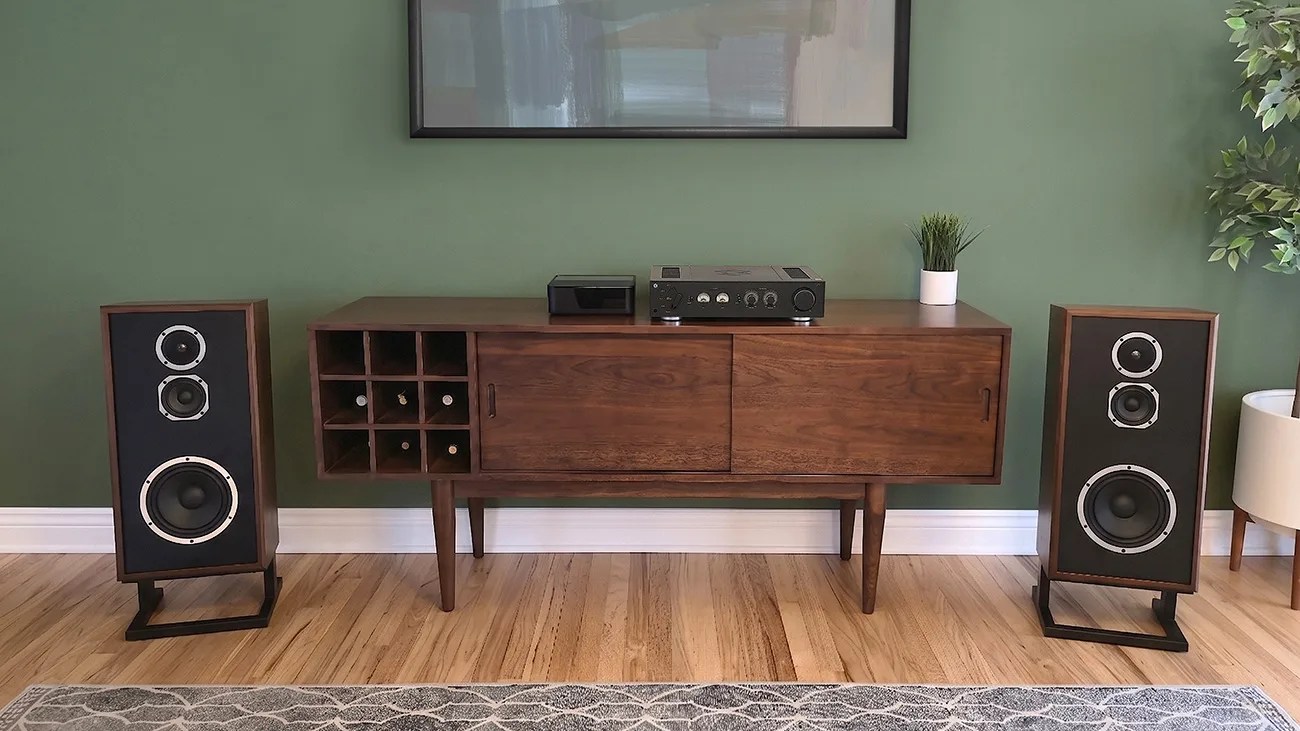 Mid-century modern wooden sideboard with built-in wine rack, vintage stereo amplifier, and two large wooden speakers on a hardwood floor.
