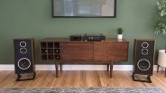 Mid-century modern wooden sideboard with built-in wine rack, vintage stereo amplifier, and two large wooden speakers on a hardwood floor.