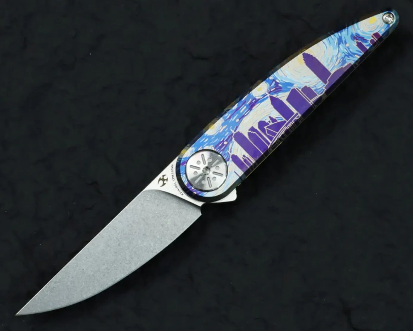 Folding knife with a stonewashed blade and a handle featuring a blue and purple city skyline design under a starry sky.
