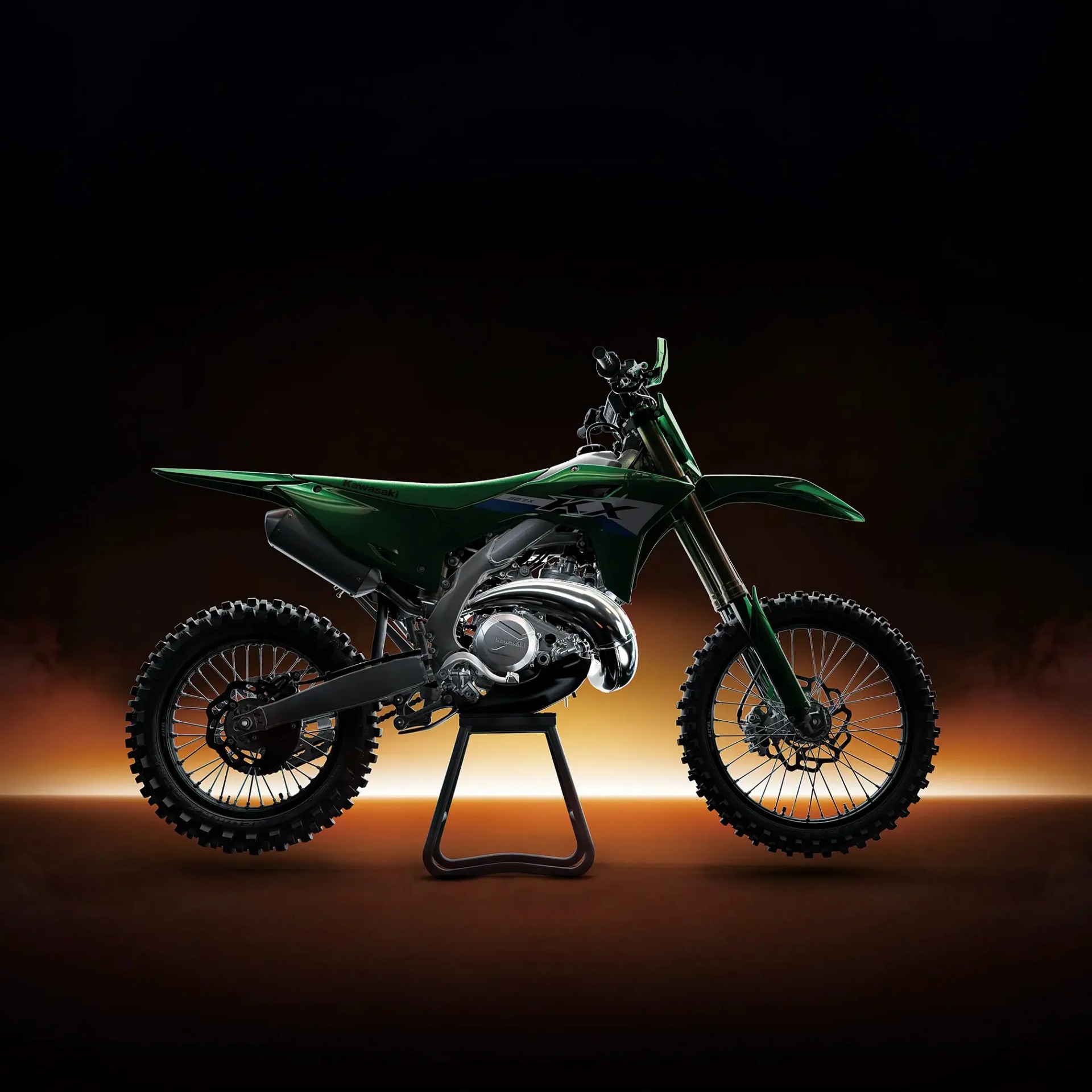 Green Kawasaki dirt bike with knobby tires on a stand against a dark background.
