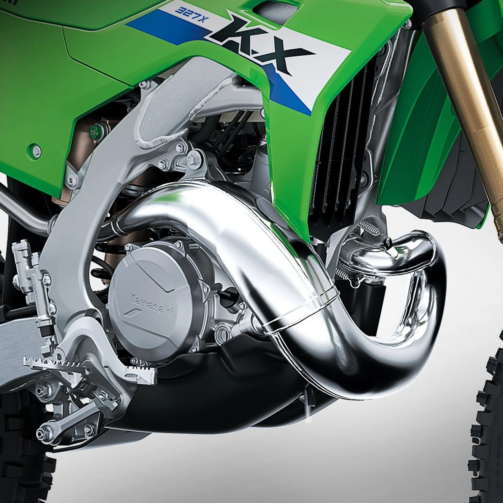 Close-up of a green Kawasaki KX 327X dirt bike engine with shiny silver exhaust pipe and front suspension fork.