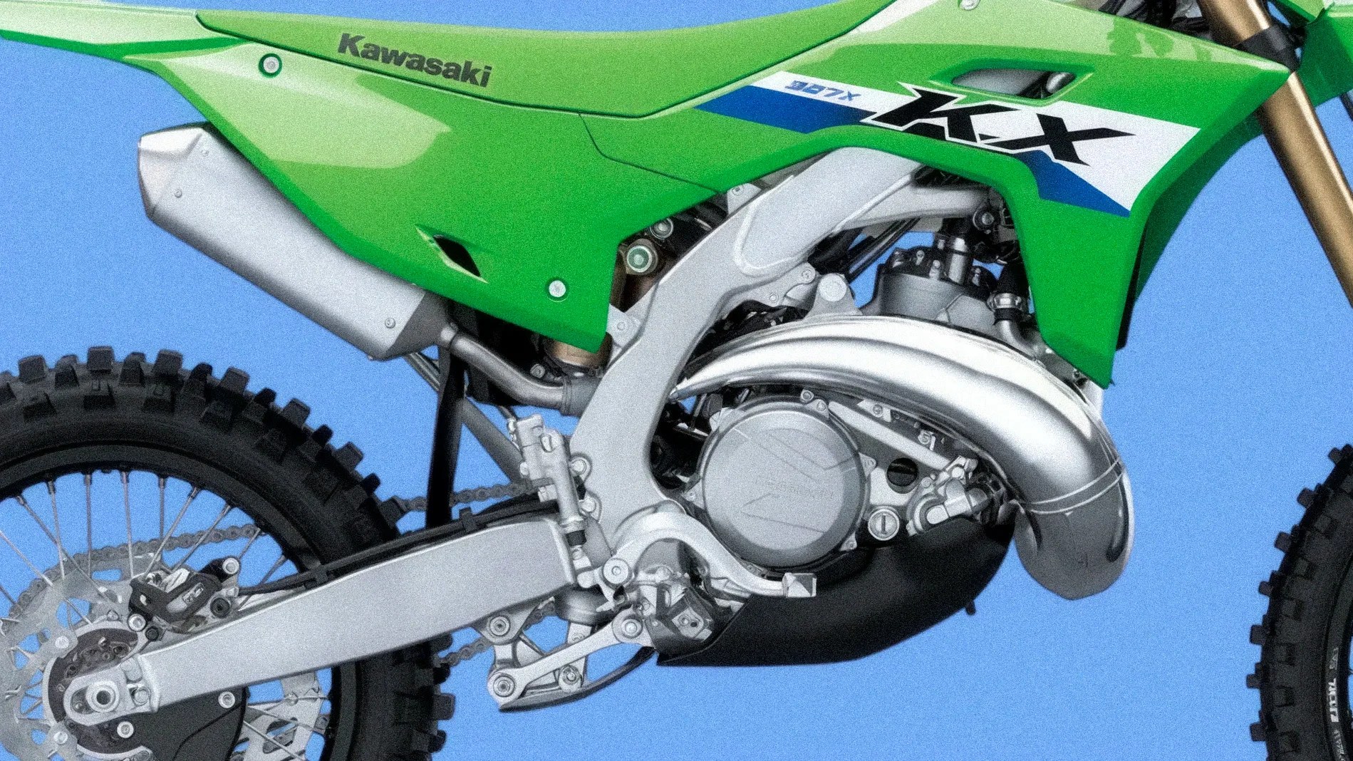 Close-up of the engine and rear wheel area of a green Kawasaki KX dirt bike against a blue background.