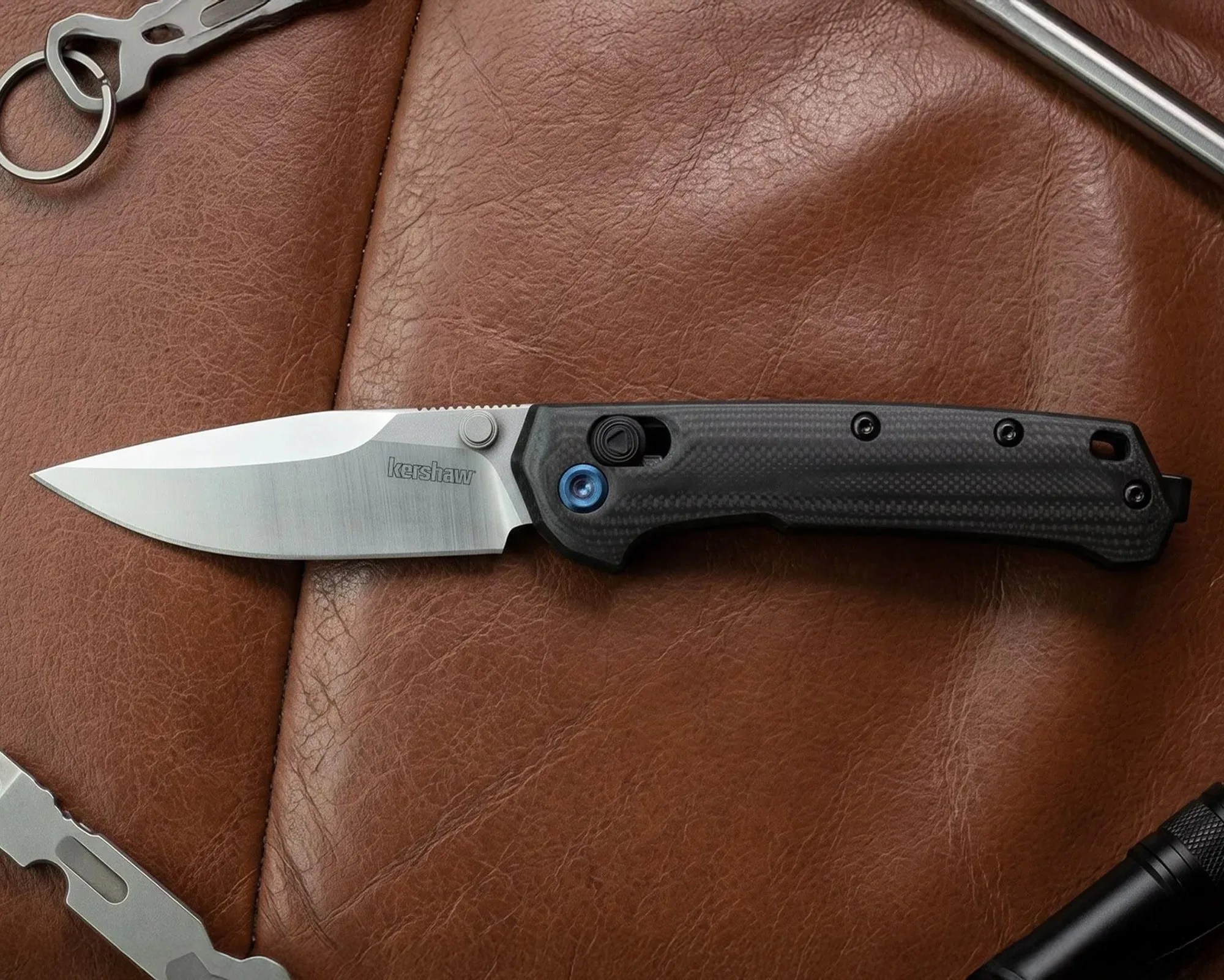 Folding Kershaw knife with a silver blade and black textured handle on brown leather.