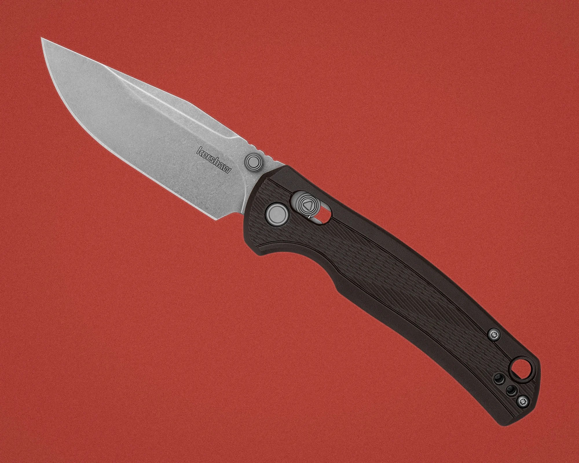 Folding knife with stonewashed blade and black textured handle on a red background.