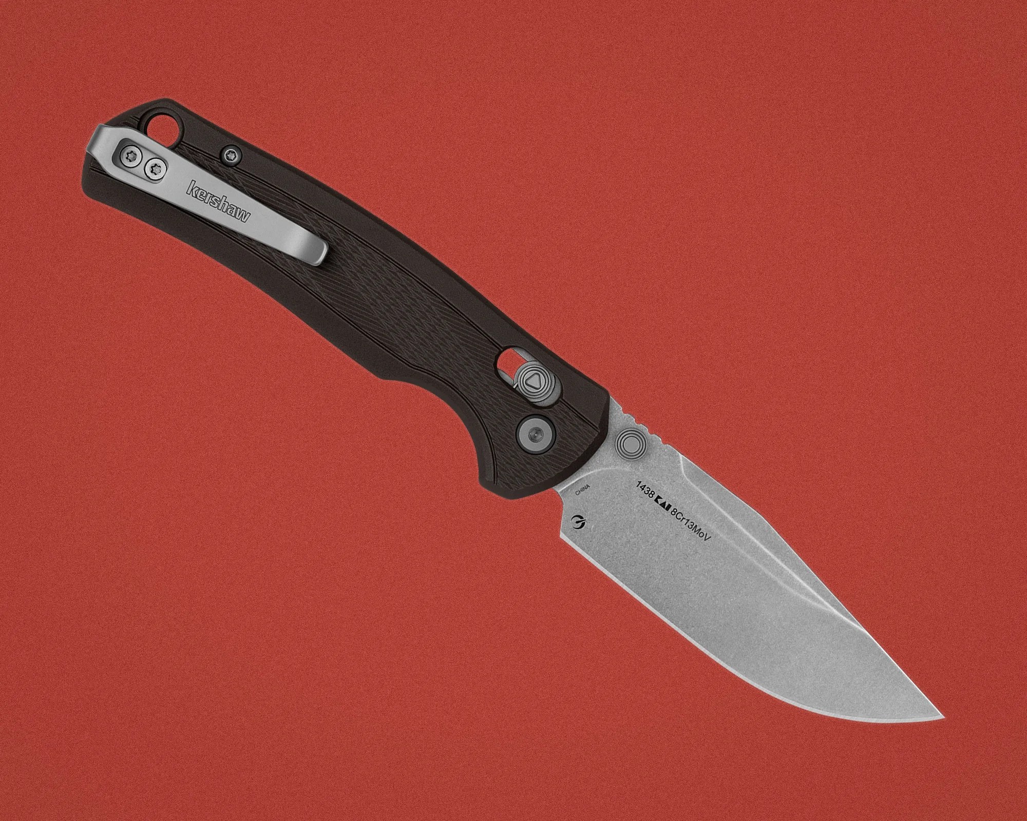 Black Kershaw folding knife handle with silver pocket clip and partially visible stonewashed blade on a red background.