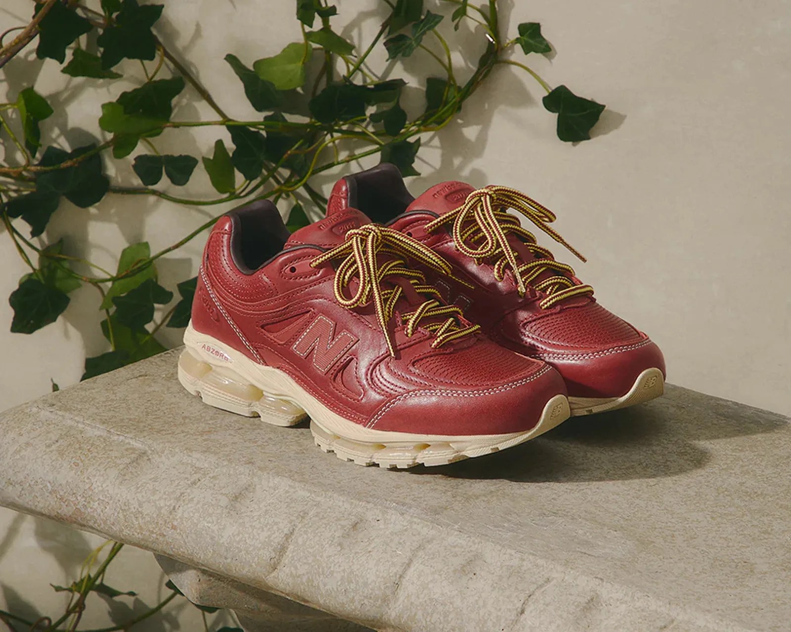Pair of red leather New Balance sneakers with yellow and black laces on a stone bench.