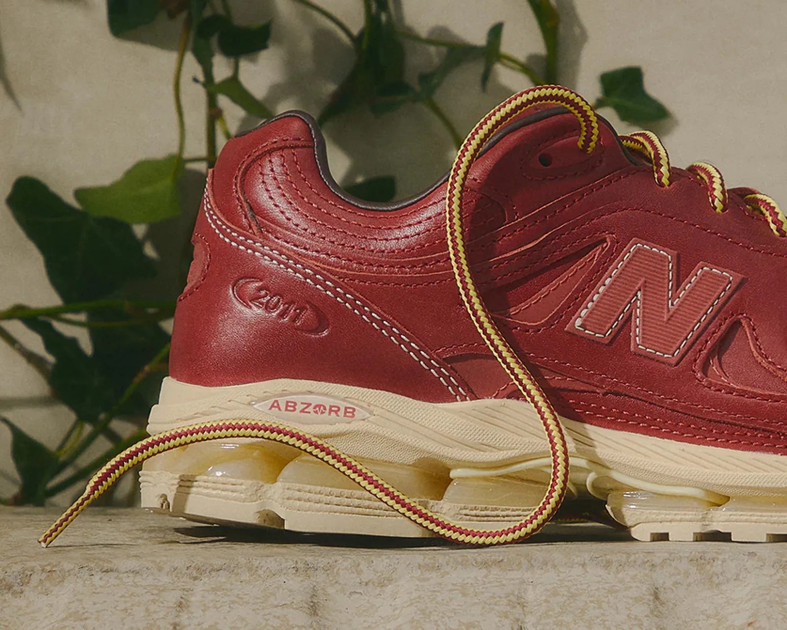 Red New Balance sneaker with yellow and red laces and beige ABZORB sole on a stone surface.