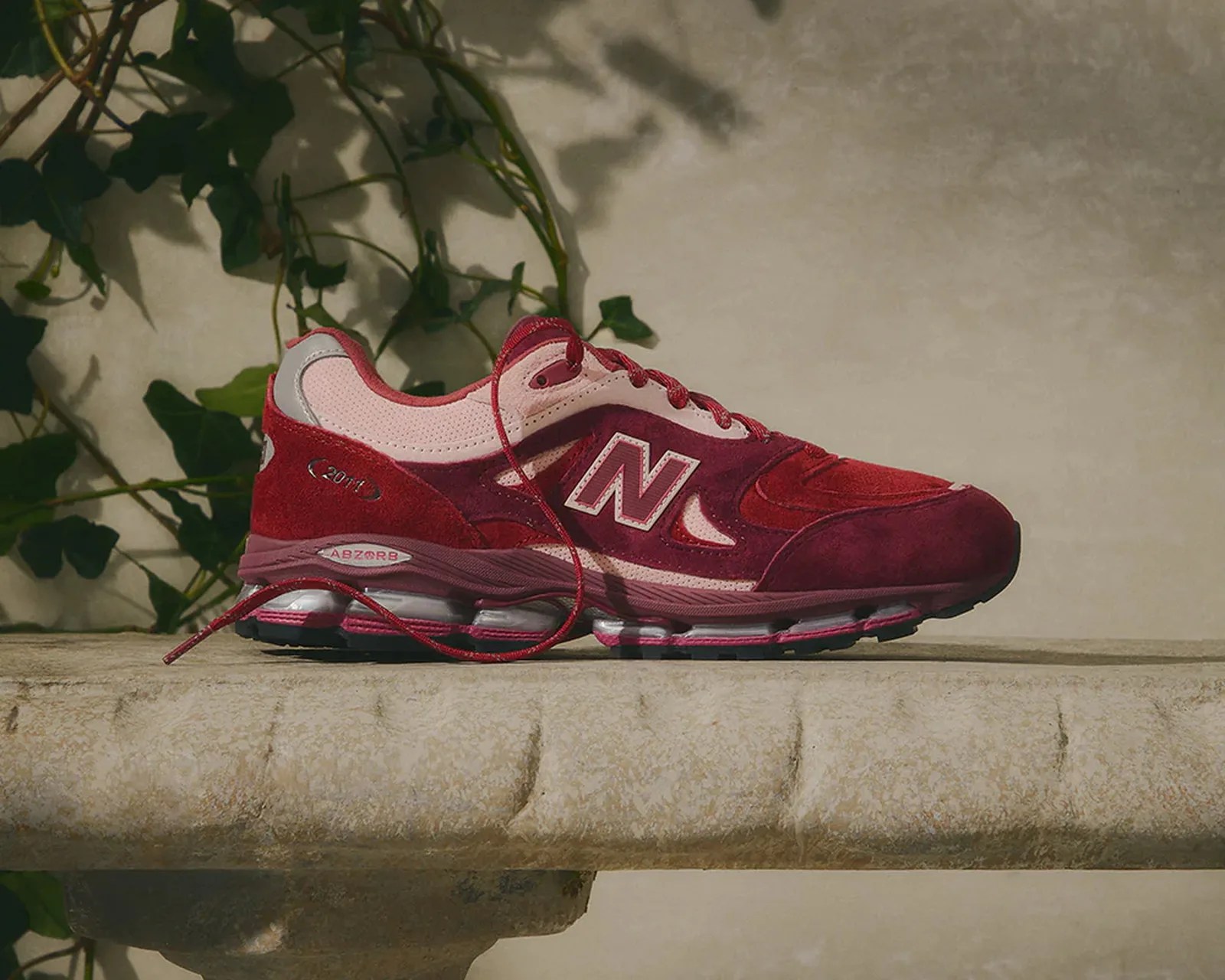 Red and pink New Balance sneaker with suede and mesh upper on a stone ledge.