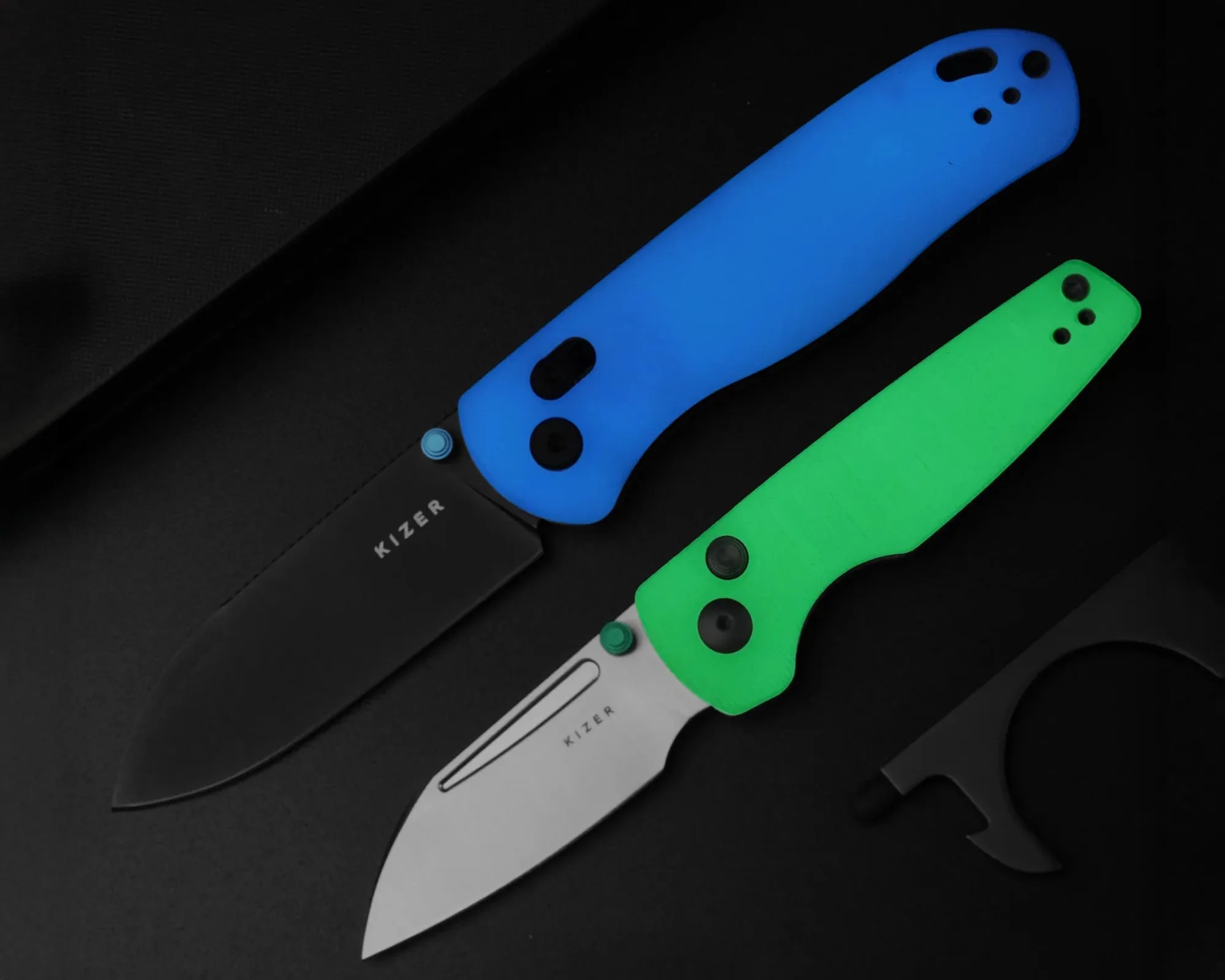 Two folding knives with blue and green handles and Kizer brand blades on a black surface.