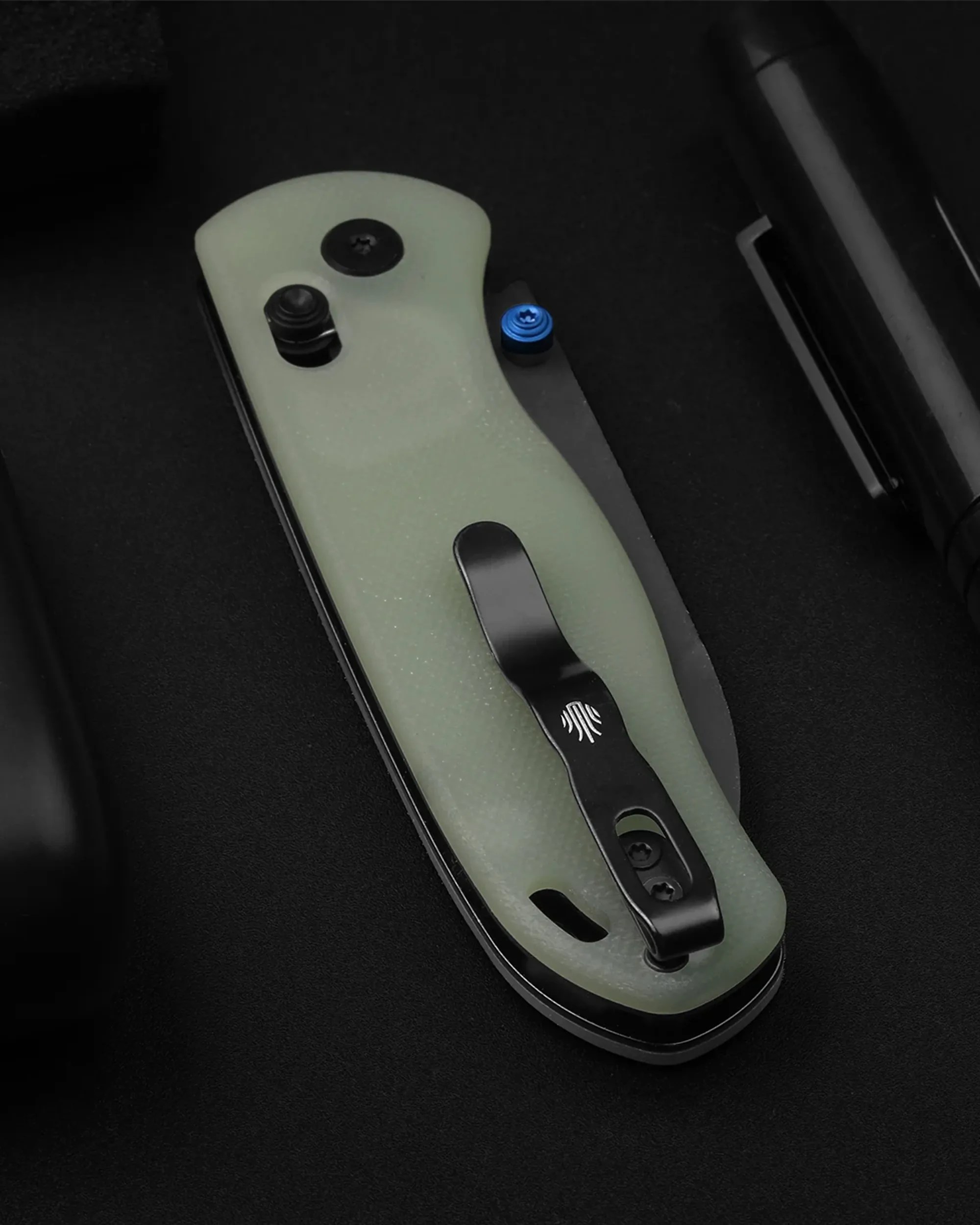 Folding knife with a translucent pale green handle, black clip, and a blue thumb stud on a black surface.