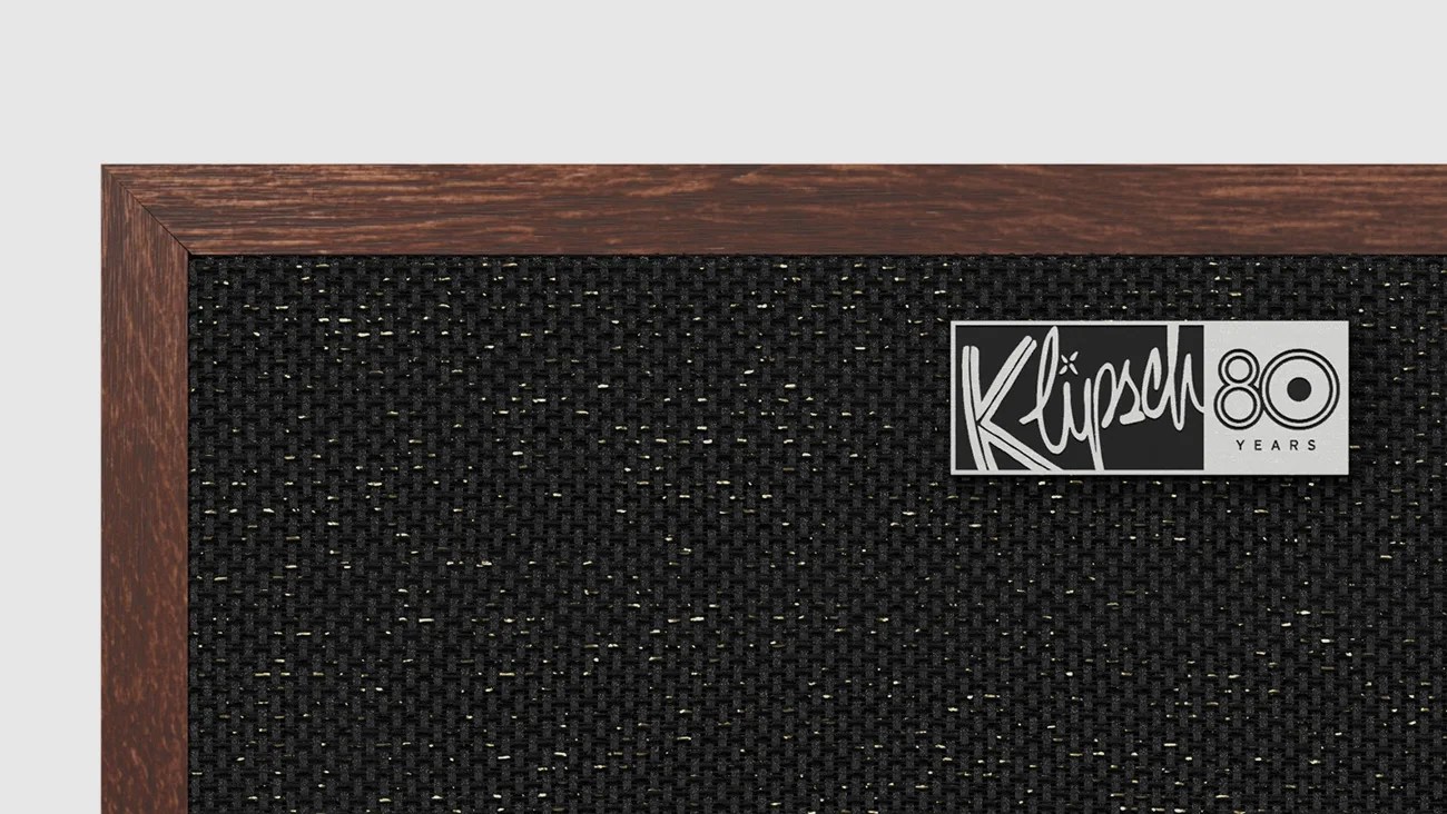 Close-up of a black woven speaker grille with a dark wood frame and a silver Klipsch 80 Years logo plaque.