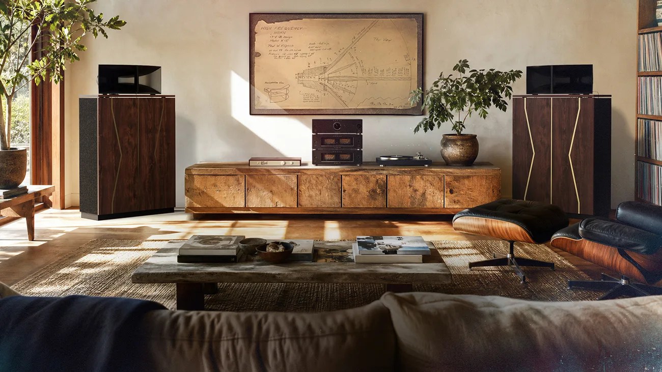 Living room with large wooden speakers, a low wooden cabinet with audio equipment, a framed schematic on the wall, and a black leather lounge chair with ottoman.