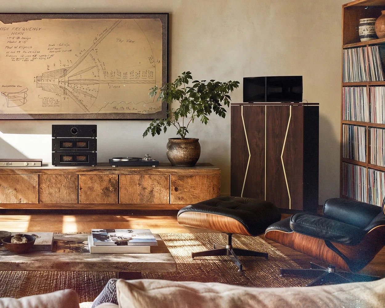 Living room with mid-century modern black leather lounge chair and ottoman, wooden media console, potted plant, and vinyl record shelf.