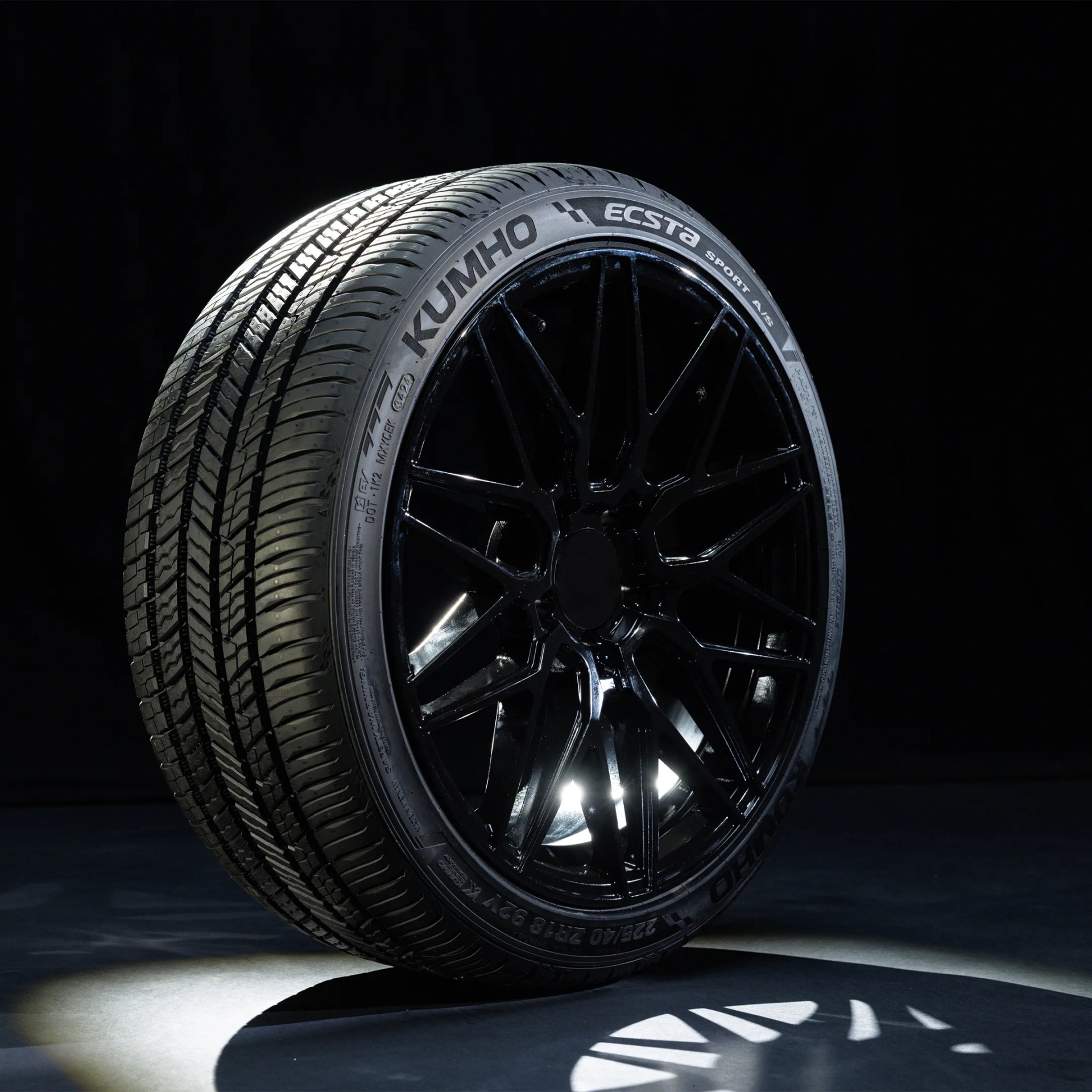 Kumho Ecsta Sport A/S tire mounted on a black multi-spoke alloy wheel with light reflection on a dark background.