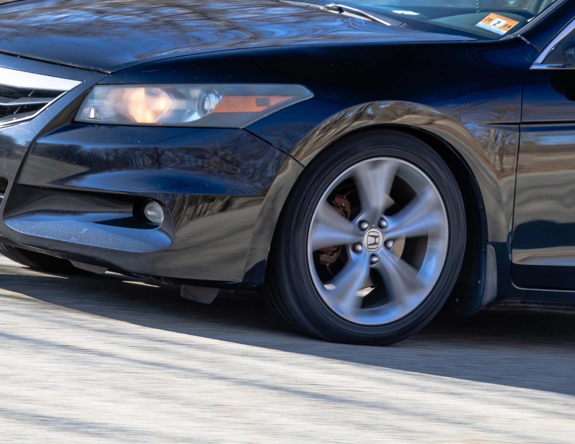 Close-up of a black Honda car front left side with spinning alloy wheel and headlight on.
