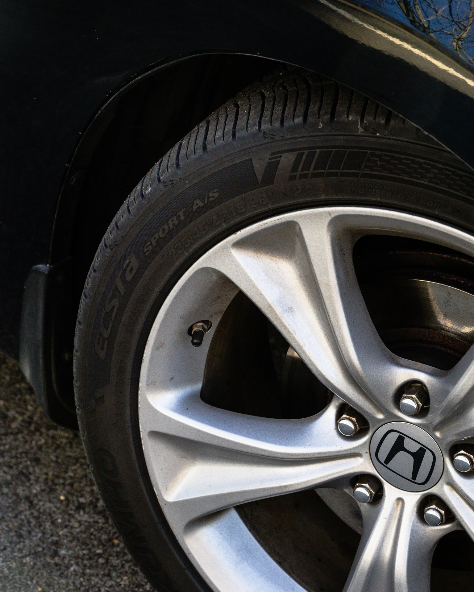 Silver alloy wheel with five spokes and a black tire on a dark-colored car.