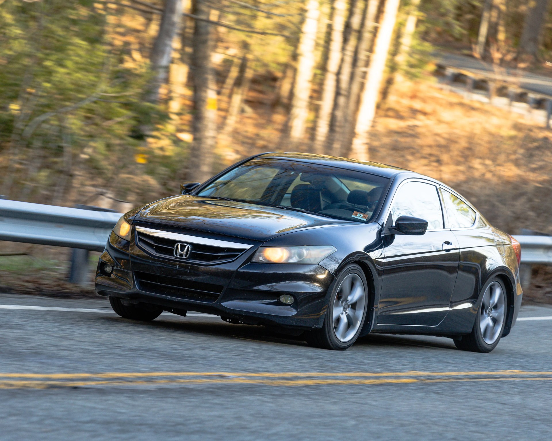 Black Honda coupe driving on a road with blurred trees in the background.