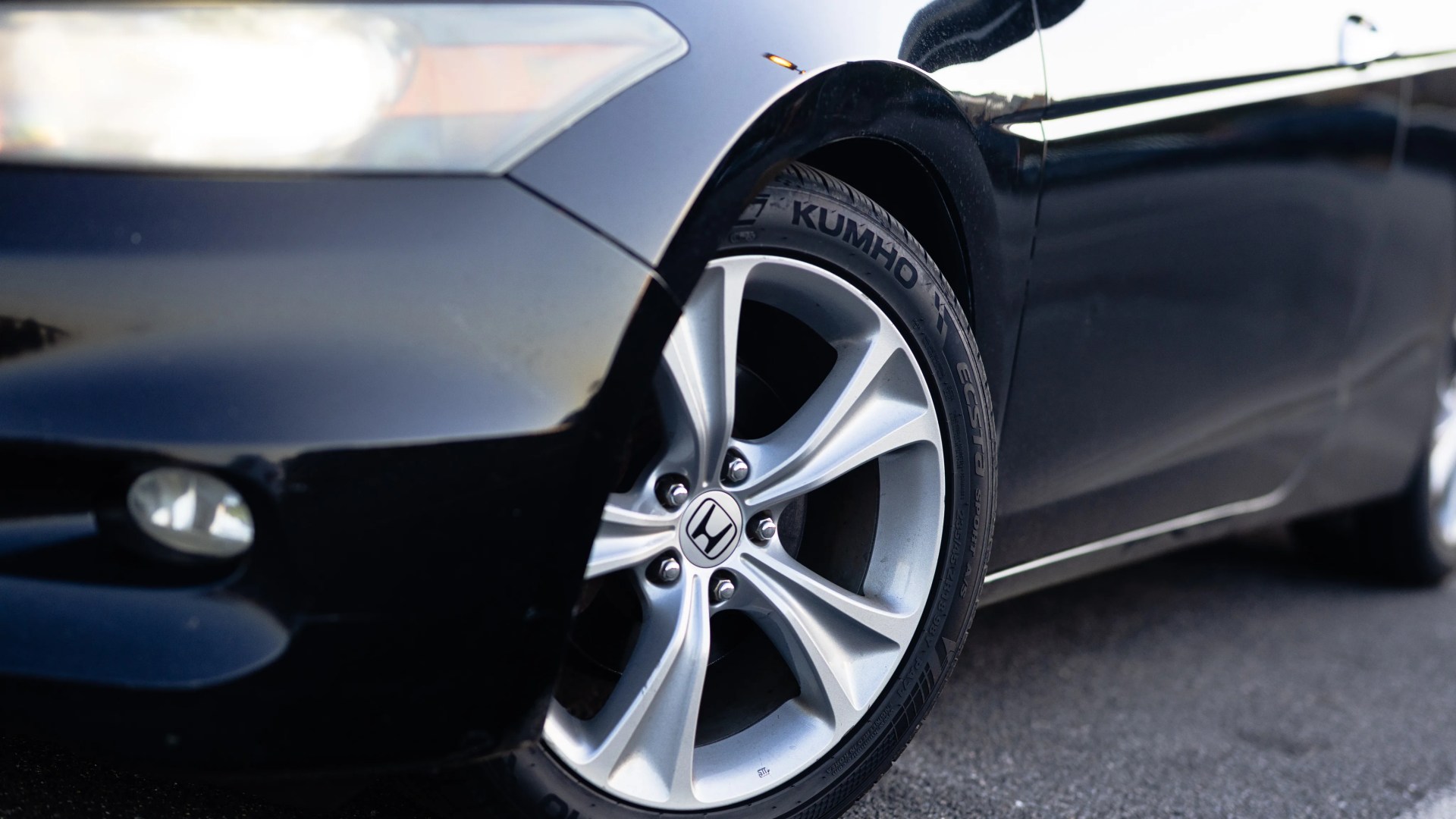 Close-up of a silver Honda alloy wheel with Kumho tire on a black car.