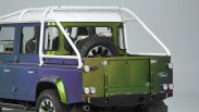 Rear side view of a two-tone blue and green Land Rover pickup with white roll cage and spare tire mounted inside the bed.