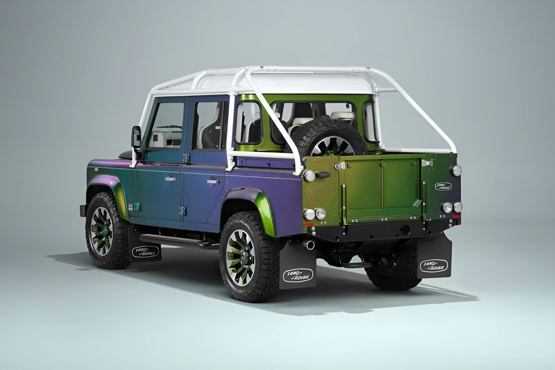Four-door Land Rover Defender with a chameleon paint finish and white roll cage in a studio setting.