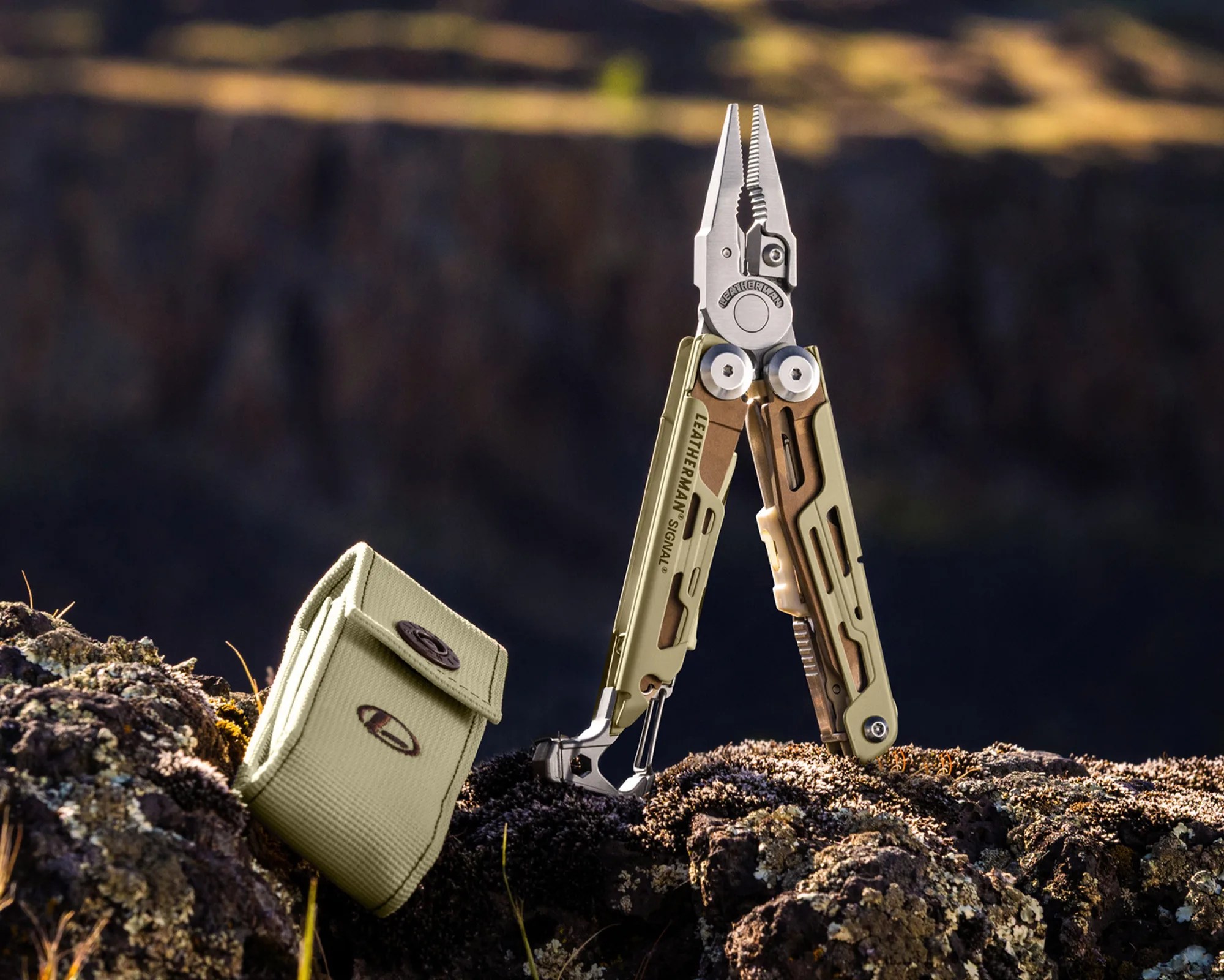 Multi-tool pliers with olive green handles standing open on rocky ground next to a matching fabric pouch.