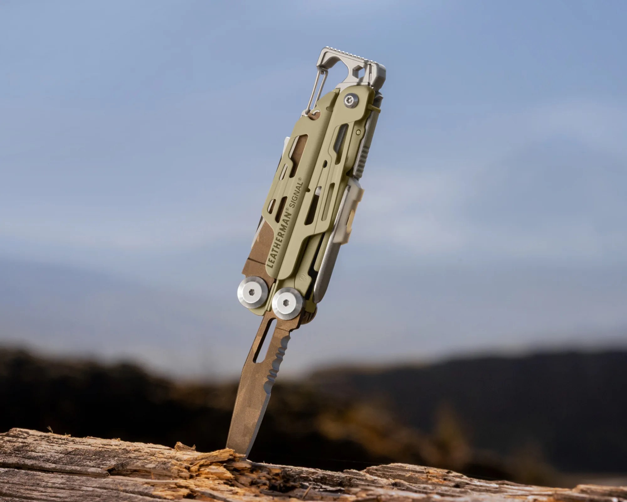 Leatherman Signal multi-tool with serrated blade stabbed into weathered wood outdoors.
