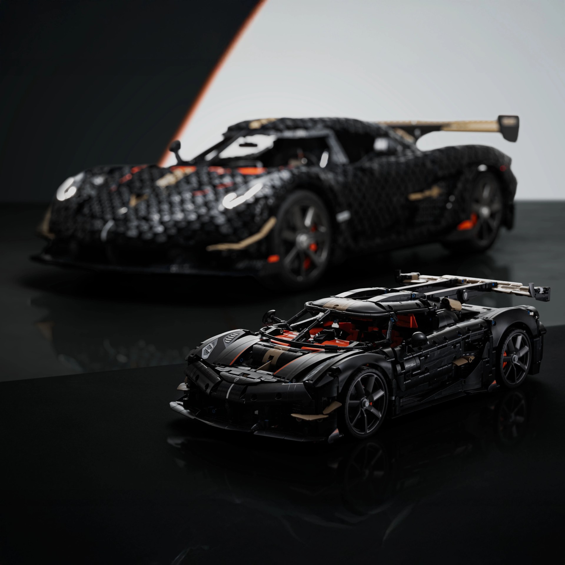 Black and tan LEGO model of a sports car with orange accents in front of a blurred similar car model.