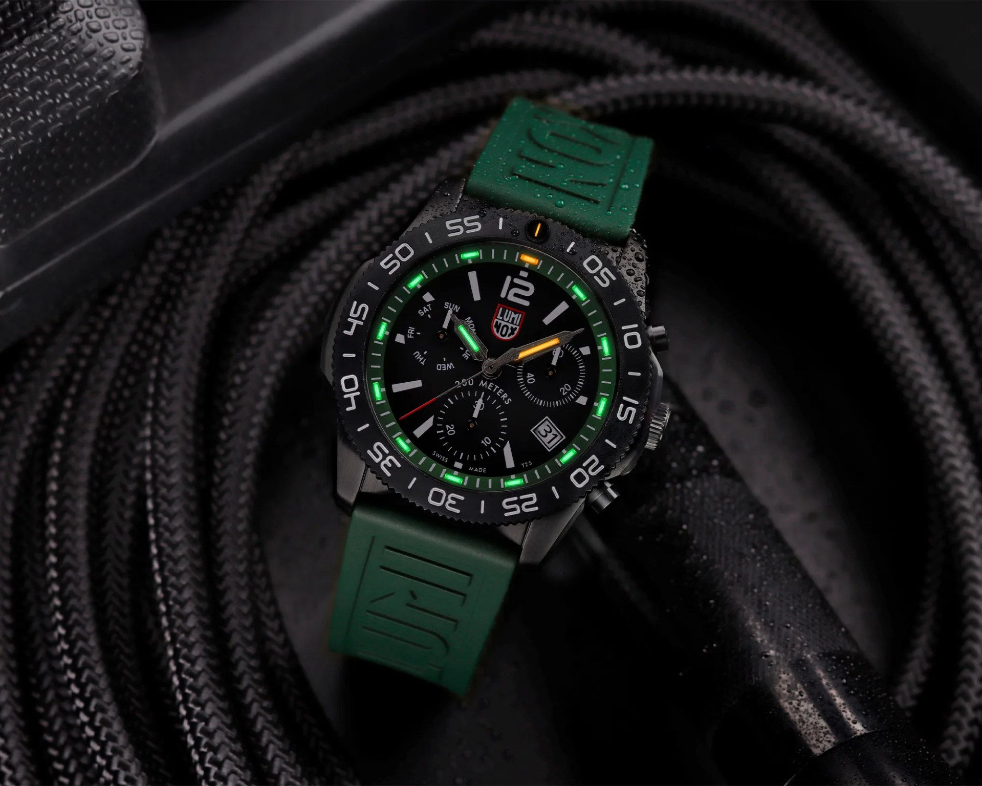 Black Luminox wristwatch with green and orange luminescent markers and a green rubber strap on a coiled black rope.