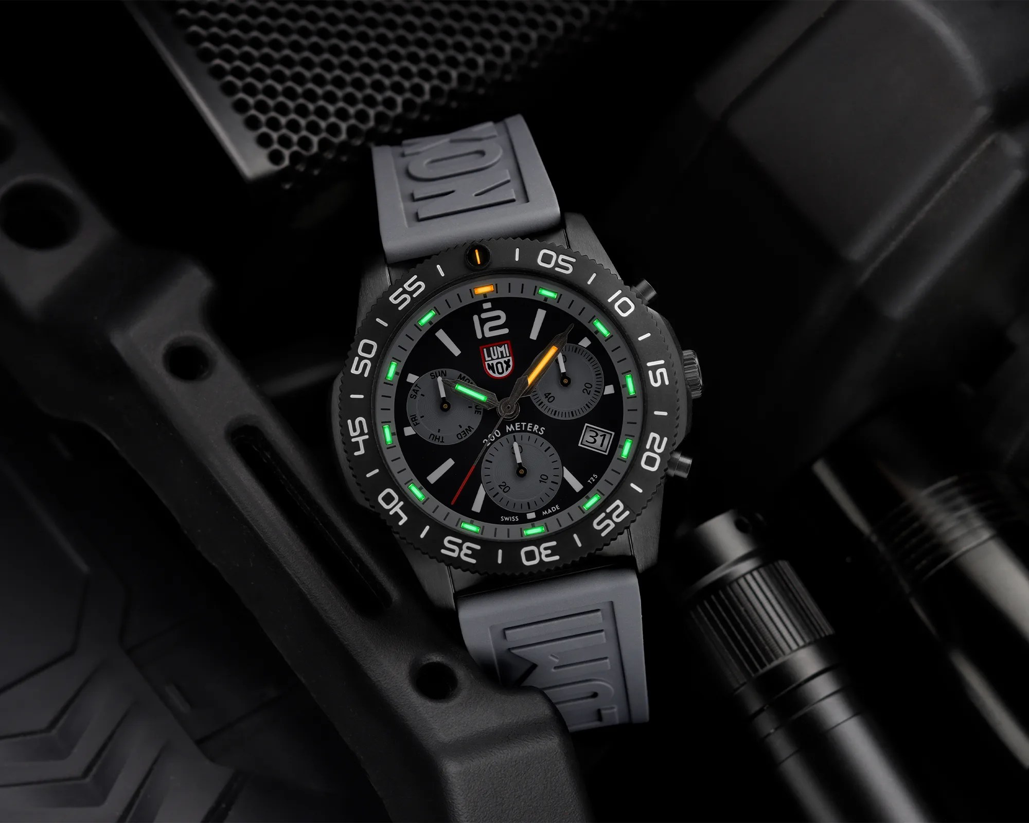 Black Luminox wristwatch with gray strap and glowing green and orange markers on a black textured surface.