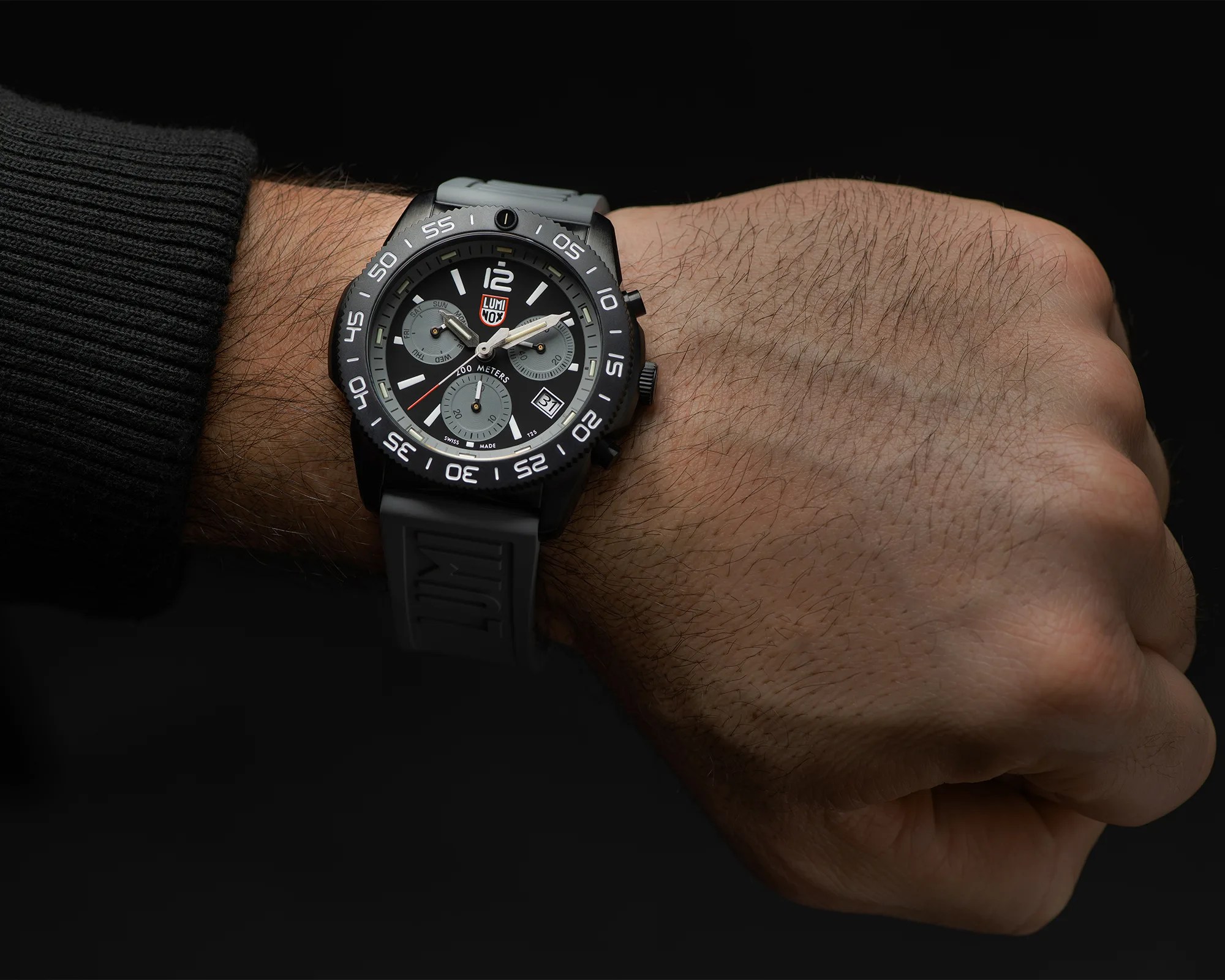 Black Luminox wristwatch with gray bezel and strap worn on a wrist against a black background.