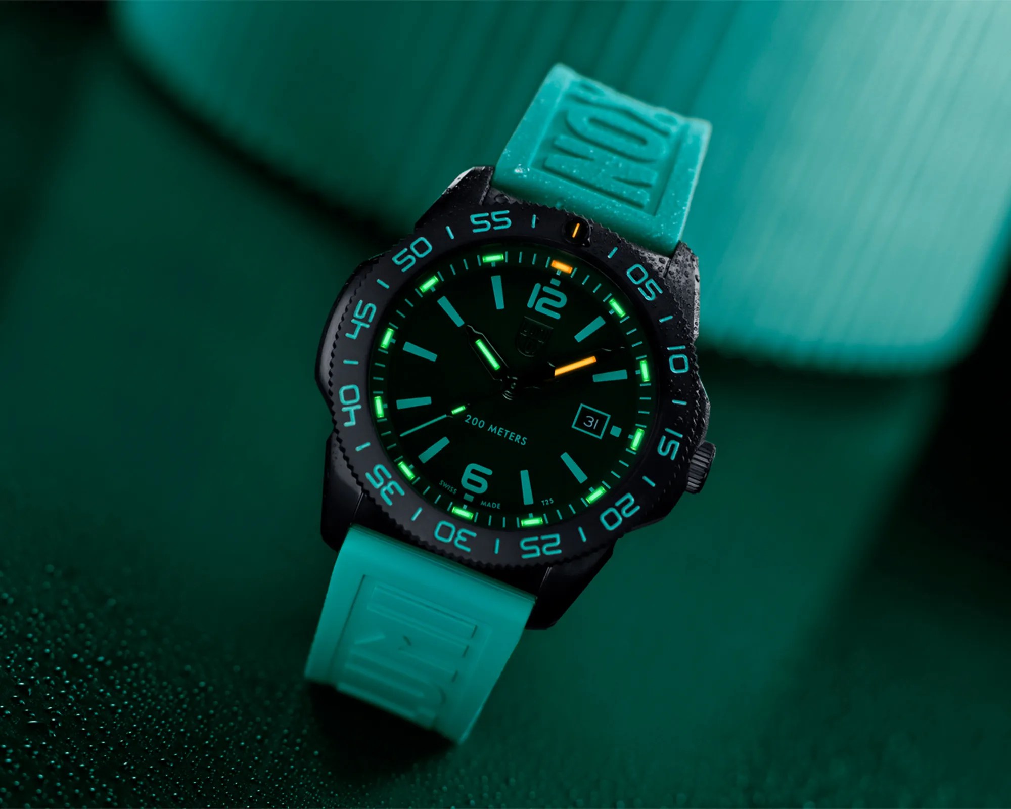 Black dive watch with glowing green and orange markers and a turquoise rubber strap on a dark green surface.