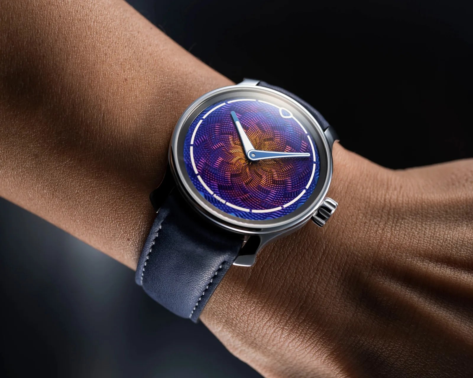 Wristwatch with a textured blue and orange dial, silver case, and dark blue leather strap worn on a wrist.