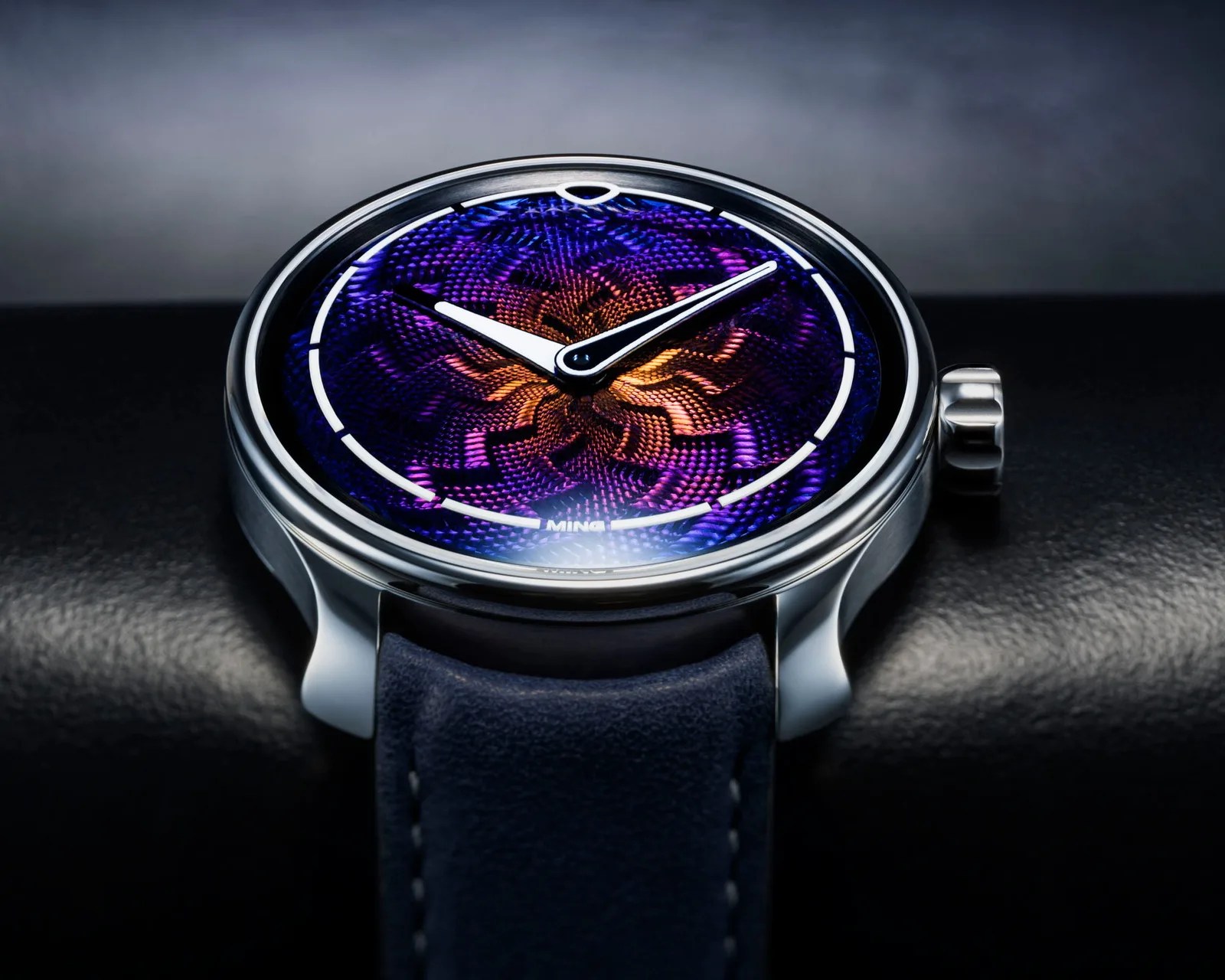 Close-up of a wristwatch with a blue and orange textured dial, white hour markers, and a blue leather strap.