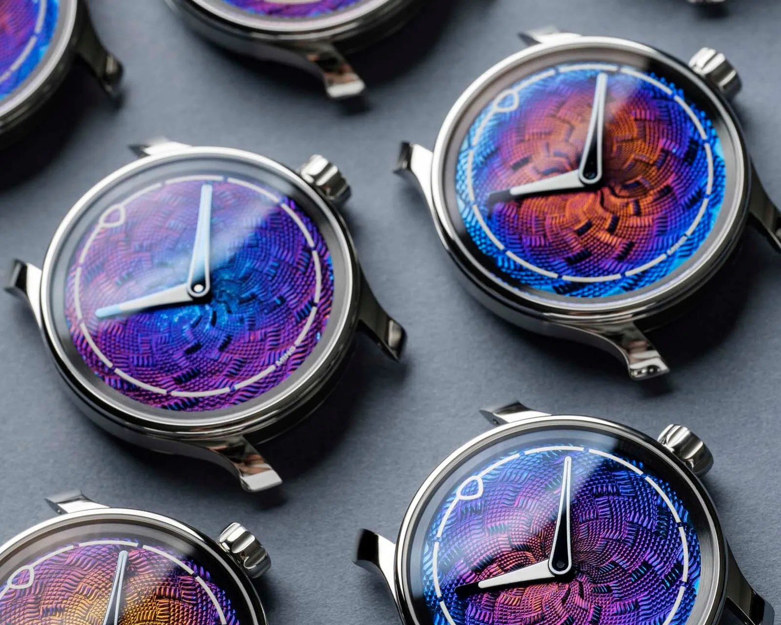 Close-up of multiple wristwatch faces with iridescent blue and purple textured dials and silver cases on a dark surface.