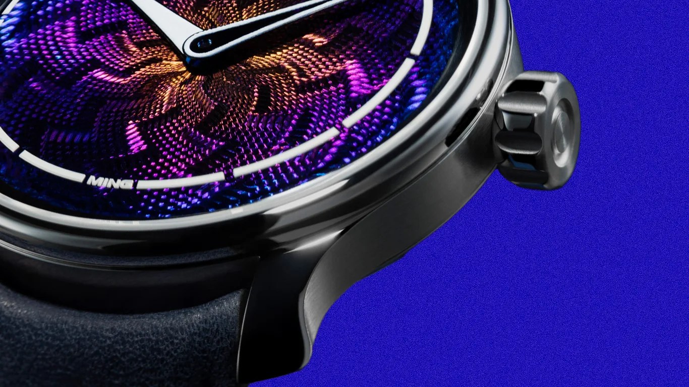 Close-up of a wristwatch with a textured purple and orange dial, silver case, and black leather strap against a blue background.