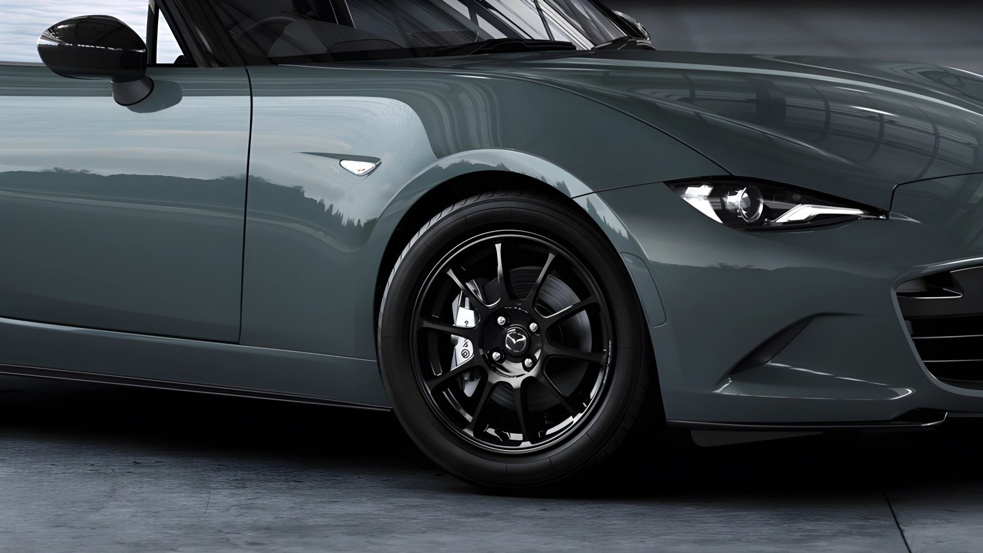 Close-up of a gray Mazda sports car front side with black alloy wheel and sleek headlight.