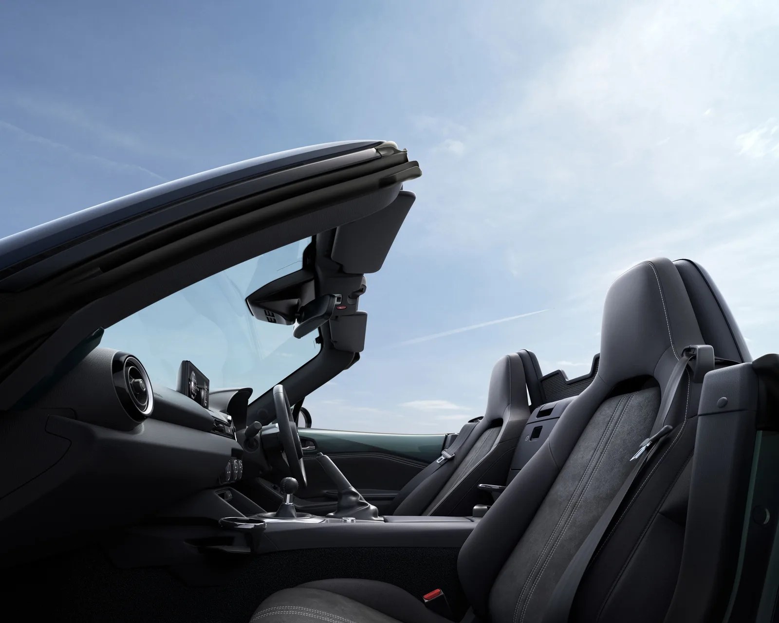 Interior of a black convertible car with leather and suede seats under a clear blue sky.