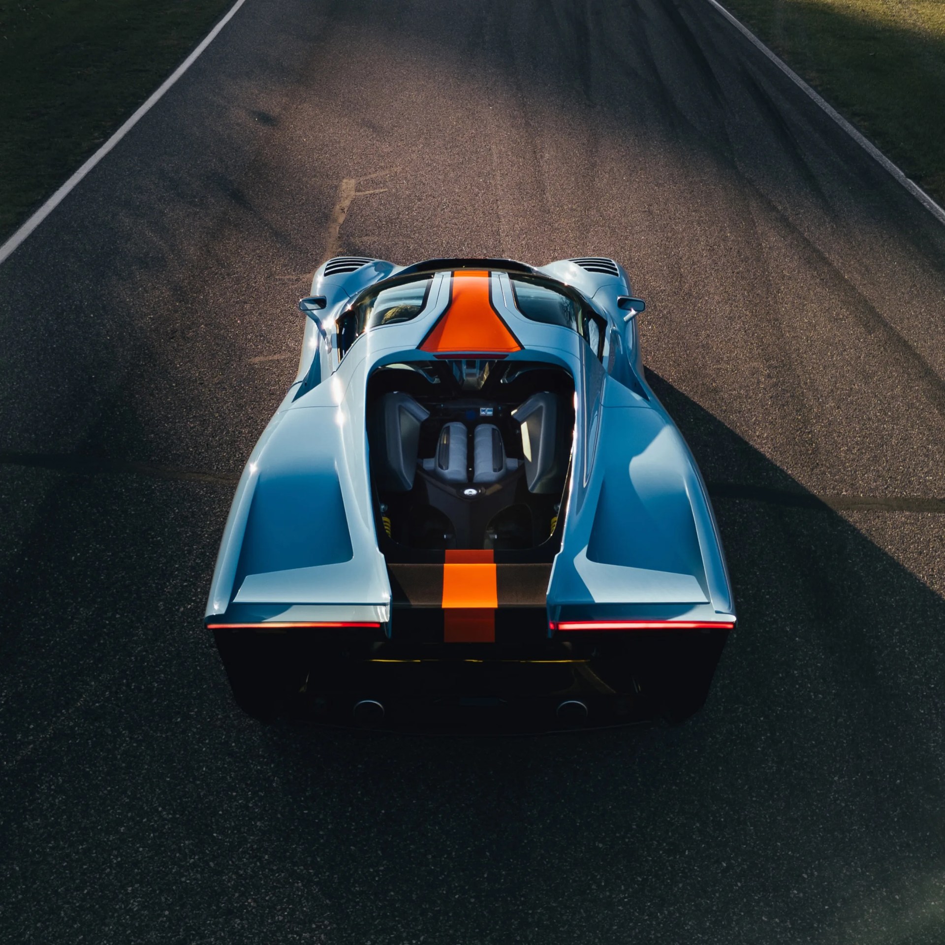 Blue sports car with an orange racing stripe viewed from above on a paved road.