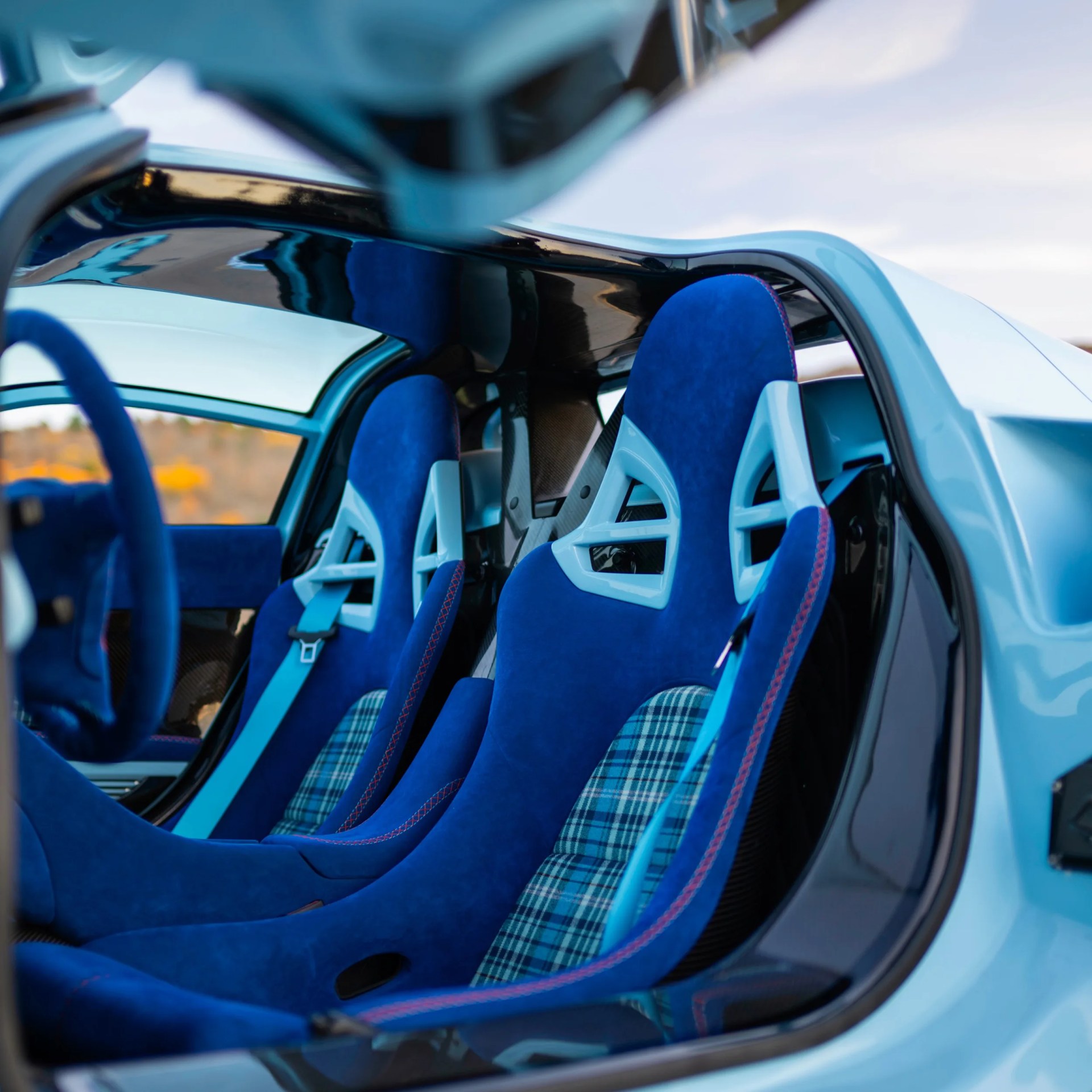 Blue racing seats with light blue frames and plaid fabric inserts inside a light blue car interior.